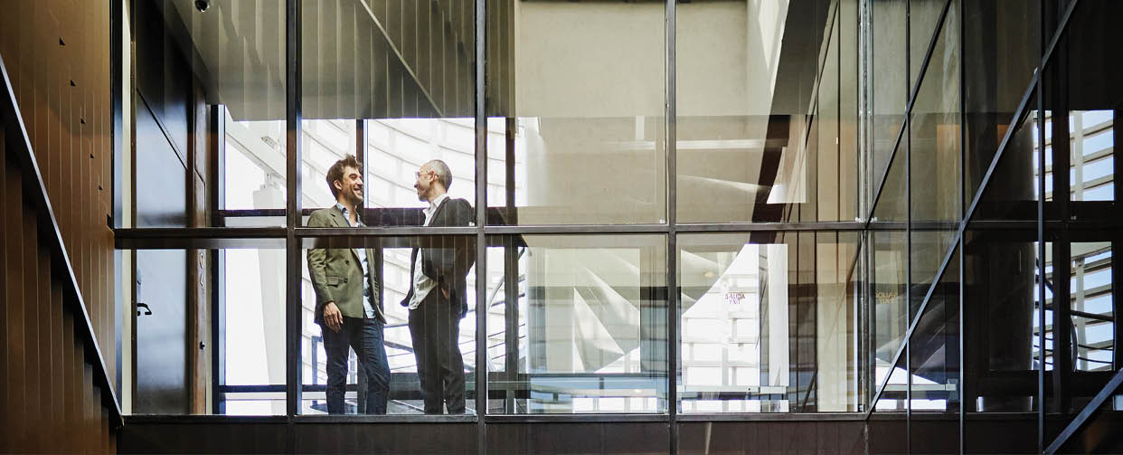 Wide shot of smiling businessmen in discussion in glass hallway of hotel during business trip